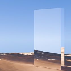 A large rectangle monolith with reflective mirrored surfaces stands in a dry desert-like location.