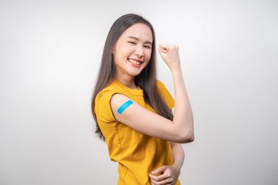 woman in yellow top with post-vaccination plaster on arm