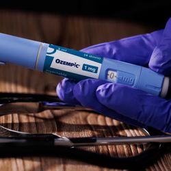 gloved hand holding an ozempic pen over a wooden table with a black stethoscope resting on it
