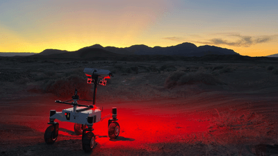 the four wheeled rover is shining a red light on the rocky desert ground at twilight