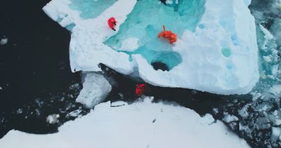 A photo looking down on three people in orange cold weather clothing moving across a melting ice burg. 