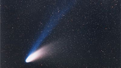 the comet has a fuzzy rugby ball appearance stretching more on one side where its tail extends, and a blue straight tail coming off it.