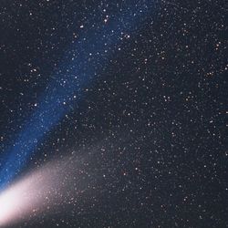 the comet has a fuzzy rugby ball appearance stretching more on one side where its tail extends, and a blue straight tail coming off it.
