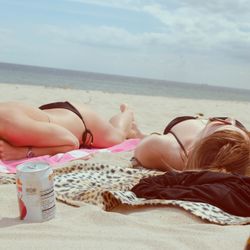 Women sunbathe on beach, sun block