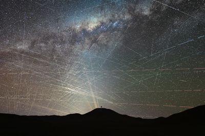 The silouhtted mountains with an observatory on top and above in the sky counteless stars and the milky way. everywhere across the sky there are satellites lines.