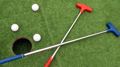 Mini golf putters, balls, and a hole on a mini golf green.