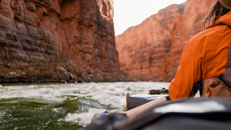 A boat floating down the Colorado River through the grand canyon, with one person in view.