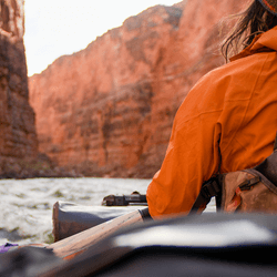 A boat floating down the Colorado River through the grand canyon, with one person in view.