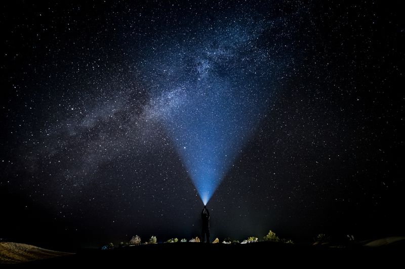 A person standing in the dark surrounded by stars, holding a torch up that is illuminating the darkness.