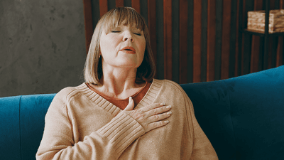 A woman on a sofa, holding her chest in apparent pain.