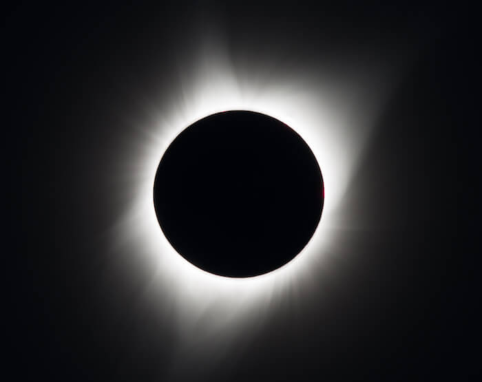 A photo of the 2017 total solar eclipse with a perfect black solid circle infront of the sun and a wispy light shown flowing out from behind it, which is the sun's corono, or atmosphere.