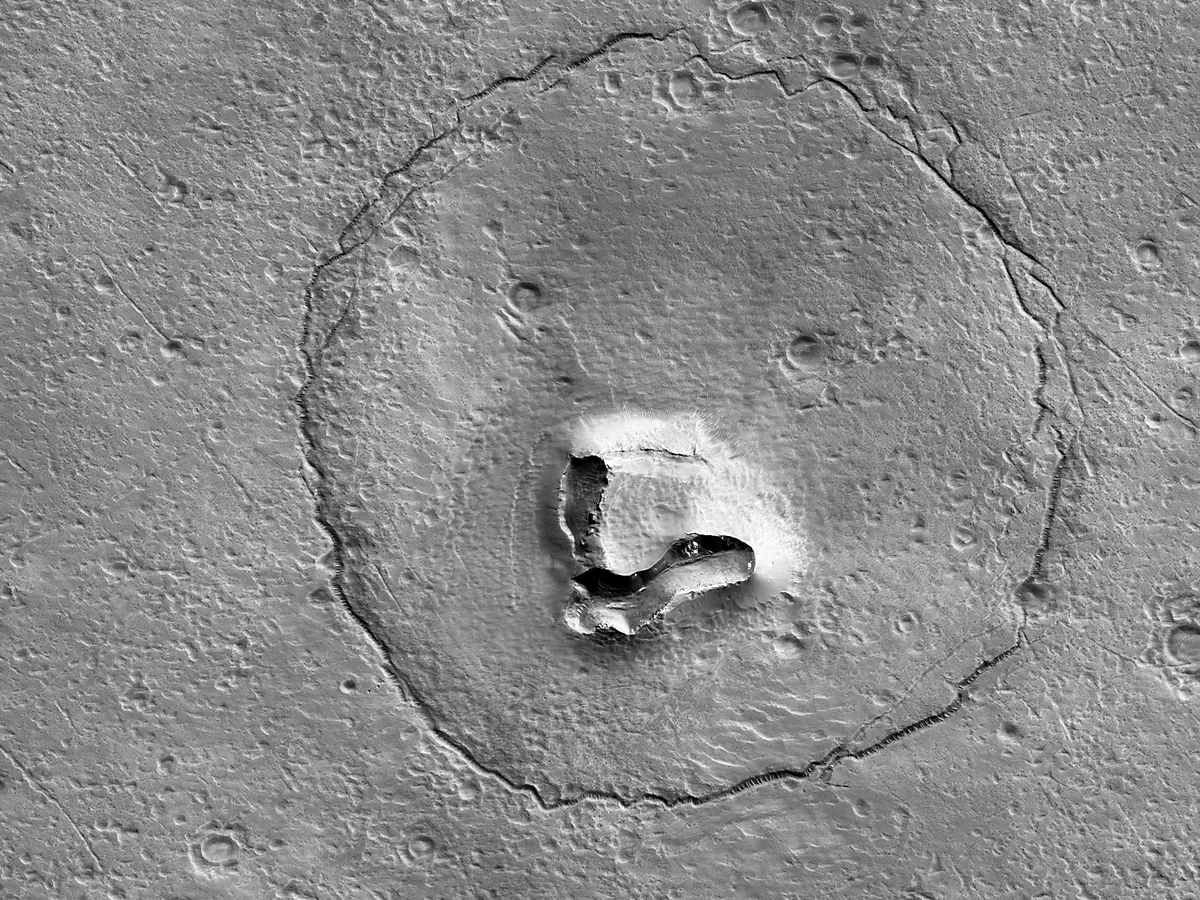 a cricrular crater with two small crater and a cental v shaped formation that looks like a round bear face