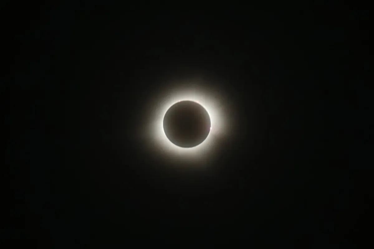 the eclipse sun and its wispy atmosphere visiblewith a few pink prominence on the rim of the Moon the eclipse sun and its wispy atmosphere visiblewith a few pink prominence on the rim of the Moon