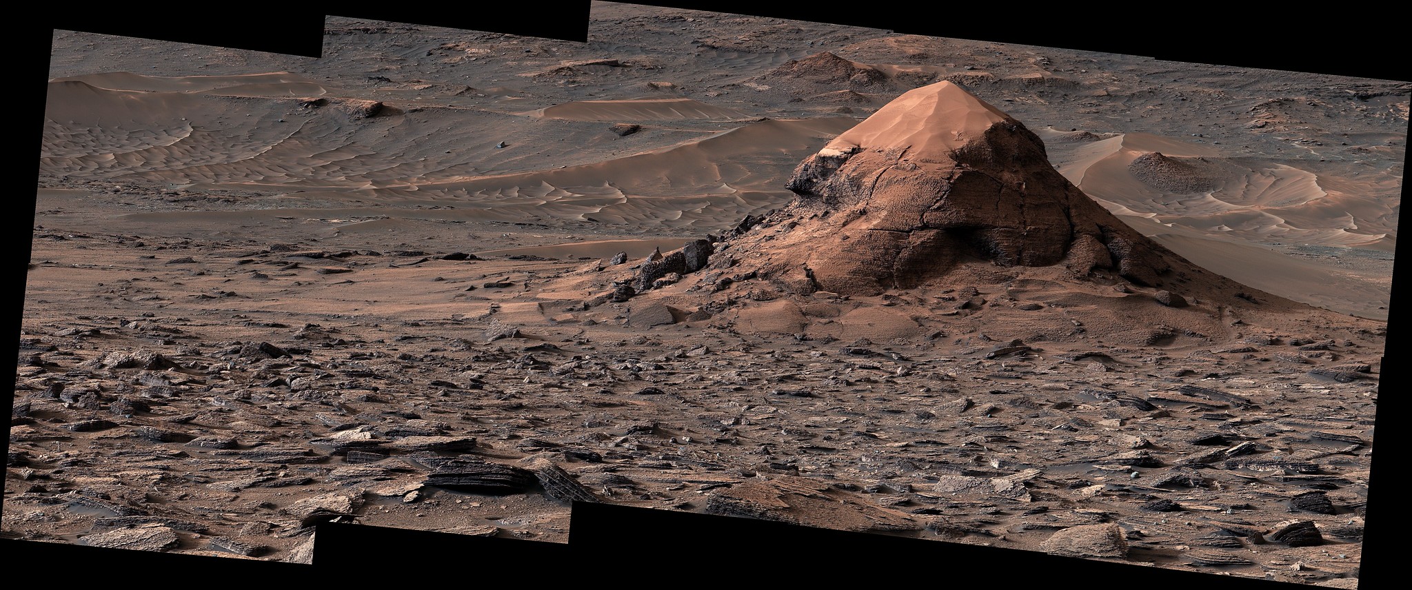 A photo of the surface of Mars with deep red-brown soil and a pointy butte- a mini moutnain-like protruding up from the ground A photo of the surface of Mars with deep red-brown soil and a pointy butte- a mini moutnain-like protruding up from the ground