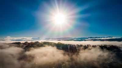Sun rise in the beautiful blue sky over misty clouds and mountain landscape.