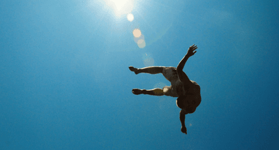 Man diving through the air, appearing to float, with a sunny blue sky background