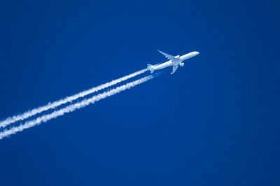 Jet plane aircraft with contrails cruising across blue sky.