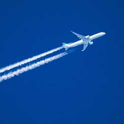 Jet plane aircraft with contrails cruising across blue sky.