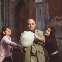 a man eating cotton candy as two young girls trying to pick some