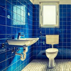 bathroom with intensely blue tiles everywhere except the floor, with two windows above the toilet, a bath on the right and a sink on the left