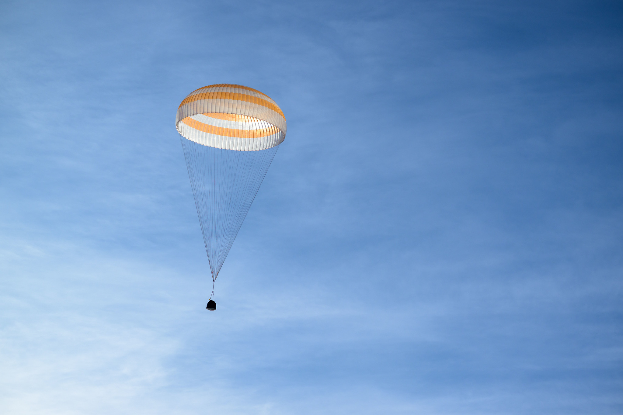 A picture of a capsule returning from the ISS with a parachute against a blue sky. 