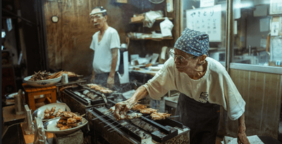 An elderly couple is cooking street food in Tokyo at night in the historic streets of Asakusa, Japan