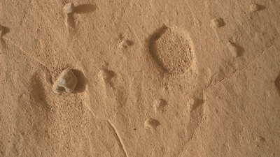 A wide, shallow pit on the surface of Mars, and a dark-toned rock nearby.