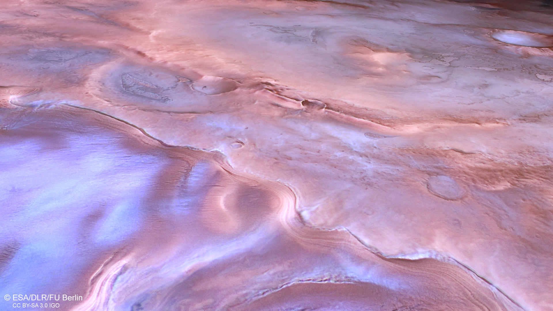 A pink-white-coloured patch of Mars, with ridges running from top left to bottom right. At the bottom left is a bright white-blue triangular patch, it looks icy. Overall, the landscape has a soft, swirly, mottled appearance A pink-white-coloured patch of Mars, with ridges running from top left to bottom right. At the bottom left is a bright white-blue triangular patch, it looks icy. Overall, the landscape has a soft, swirly, mottled appearance
