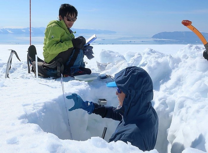 Two researchers have dig a hole in the ice to measure changes. One is standing in it. Two researchers have dig a hole in the ice to measure changes. One is standing in it.