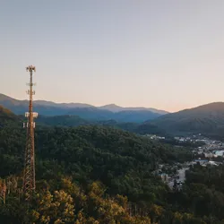 tall cell tower emerging from a forest with mountains in the background