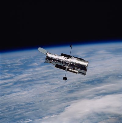 the hubble space telescope, a long silver cilynder, with the Earth behind it