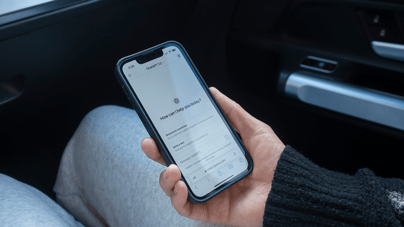 A phone loaded with ChatGPT, held by a hand in a car.