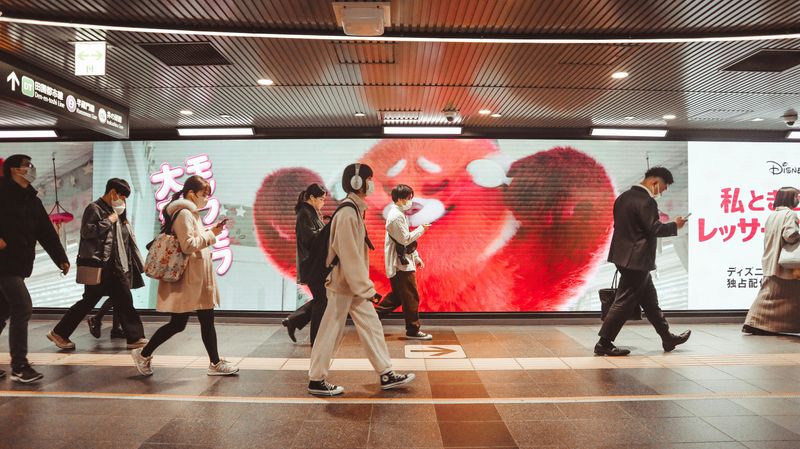 People walking in front of a huge LED monitor screen at Shibuya Station in Tokyo, Japan.