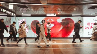 People walking in front of a huge LED monitor screen at Shibuya Station in Tokyo, Japan.