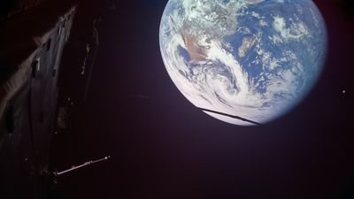 Mostly black space, most of Earth visible at the top right of the image. Part of a spacecraft visible on the left.