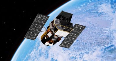 a boxy telescope with solar panels on both sides seen above Earth
