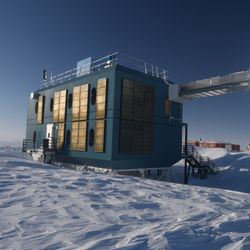 A boxy bulding connected to a cylindrical structure over the icy landscape of Antarctica