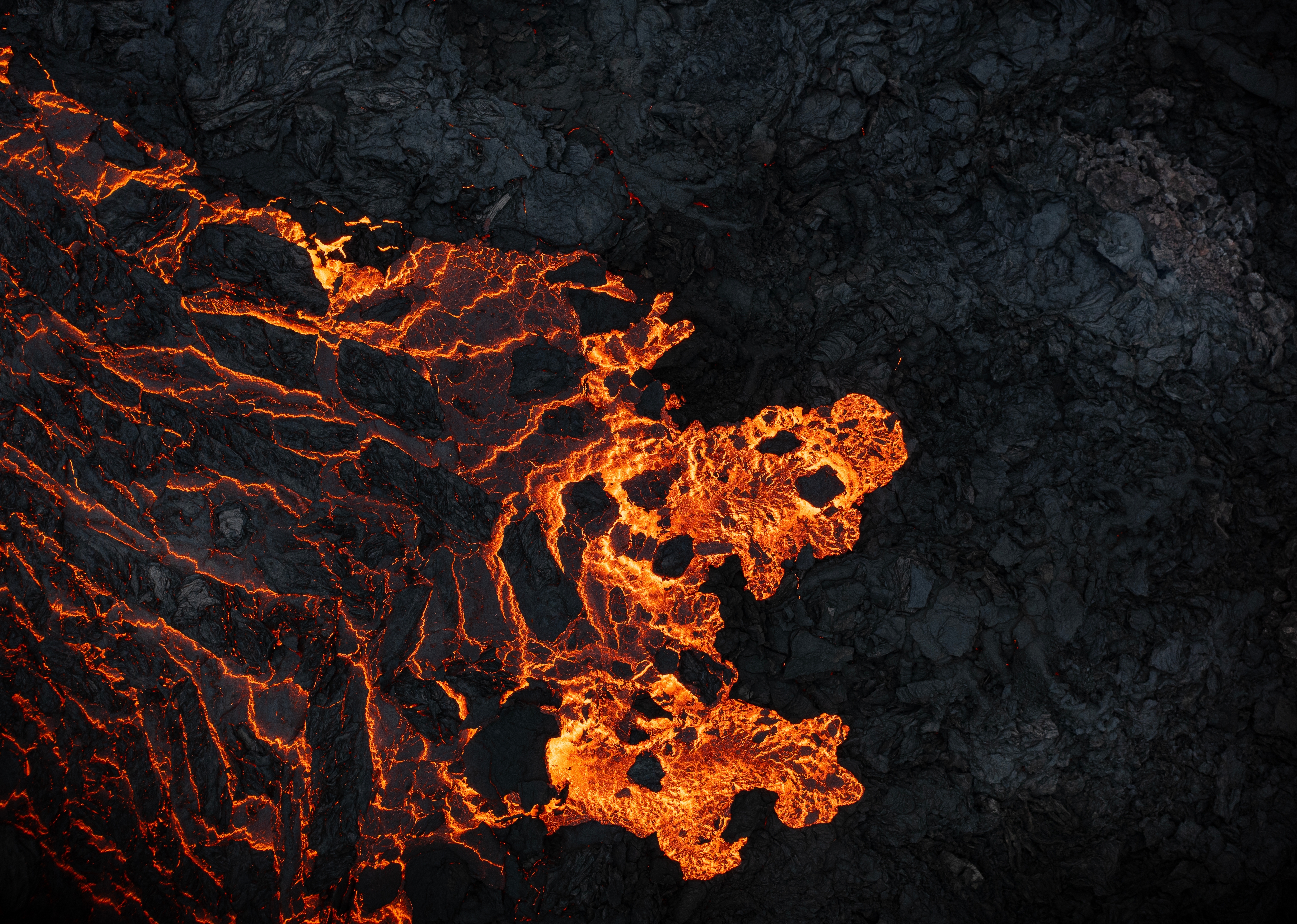 A top down view of glowing lava flowing across black rocks. A top down view of glowing lava flowing across black rocks.