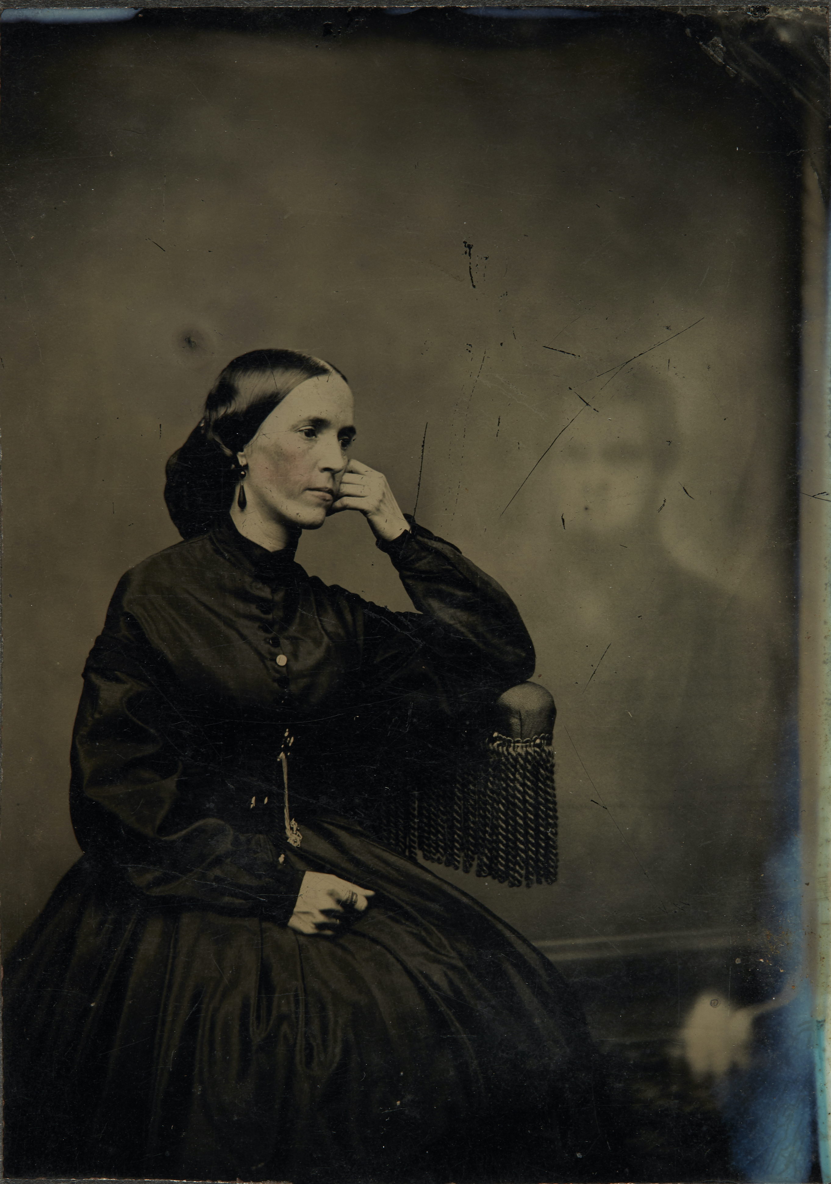 black and white photograph of a woman in victorian dress with the faint ghost image of a man beside her