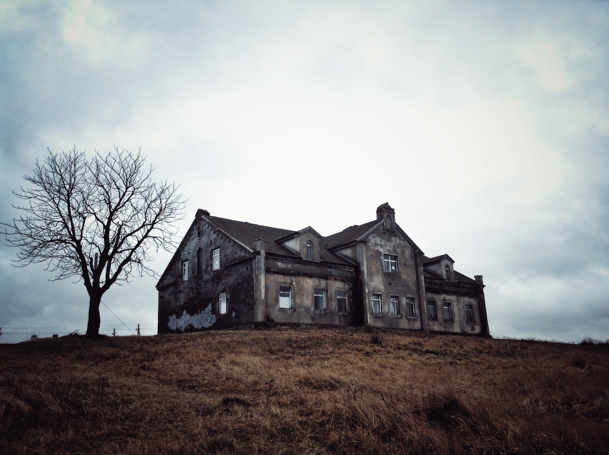 A grey, abandoned house on the top of a hill. A grey, abandoned house on the top of a hill.