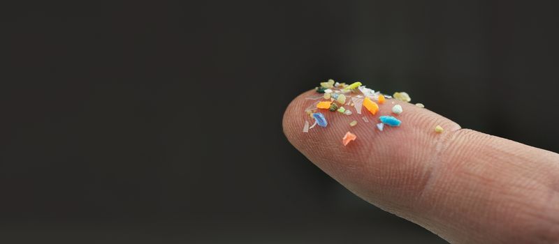 A human finger on which are a range of brightly coloured tiny pieces of plastic.