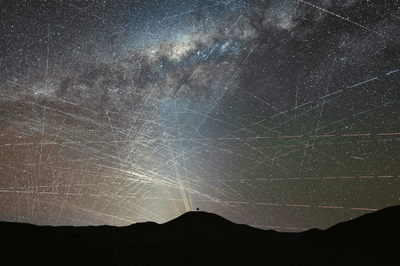 The silouhtted mountains with an observatory on top and above in the sky counteless stars and the milky way. everywhere across the sky there are satellites lines.